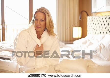 Stock Image - Woman wearing bathrobe on bed. Fotosearch