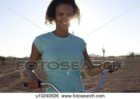 Stock Photograph - Woman with bicycle in desert landscape. Fotosearch