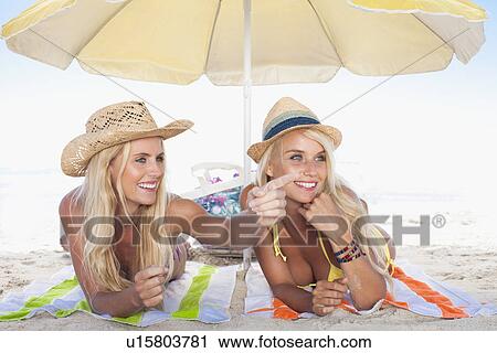 Stock Image - Women relaxing under umbrella on beach. Fotosearch