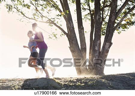 Stock Photograph - Women running together on dirt path. Fotosearch