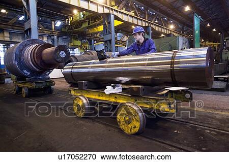 Stock Image - Worker cleaning metal in steel forge. Fotosearch
