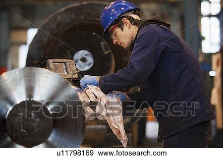 Stock Photo - Worker cleaning metal in steel forge. Fotosearch