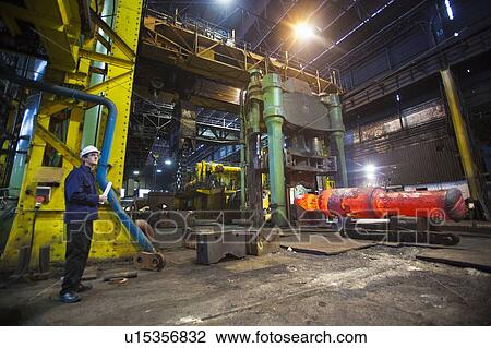 Stock Image - Worker standing in steel forge. Fotosearch