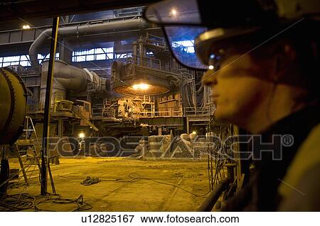 Stock Photo - Worker standing in steel forge. Fotosearch