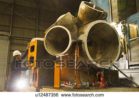 Stock Photograph - Worker using machinery in steel forge. Fotosearch
