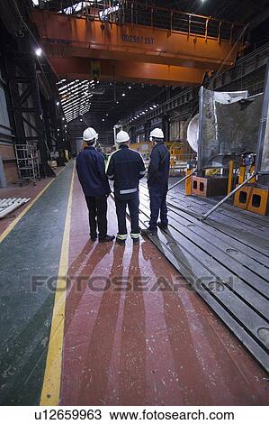 Stock Image - Workers talking in steel forge. Fotosearch