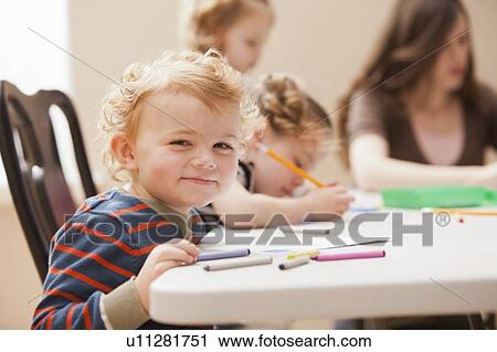 Stock Image - Boy (4-5) looking at camera during art lesson in kindergarten. Fotosearch