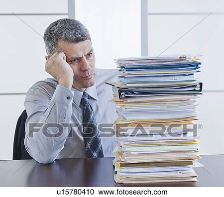 Stock Image - Businessman looking at large stack of documents. Fotosearch
