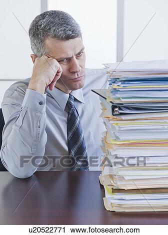 Businessman looking at large stack of documents View Large Photo Image Stock Image - Businessman looking at large stack of documents. Fotosearch