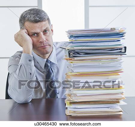 Businessman sitting next to large stack of documents View Large Photo Image Stock Image - Businessman sitting next to large stack of documents. Fotosearch