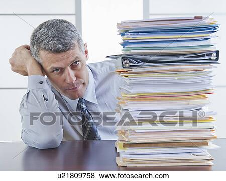 Stock Photo - Businessman sitting next to large stack of documents. Fotosearch