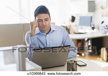 Stock Image - Businessman working on laptop, businesswoman in background. Fotosearch