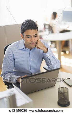 Stock Photograph - Businessman working on laptop, businesswoman in background. Fotosearch