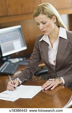 Stock Image - Businesswoman writing at desk. Fotosearch