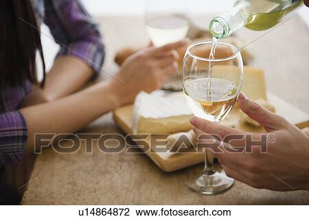 Stock Image - Close up of couple pouring wine and dining. Fotosearch