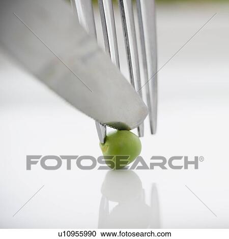 Stock Image - Close up of knife, fork and green pea, studio shot. Fotosearch