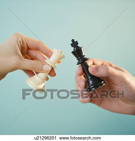 Stock Image - Close up of man's and woman's hands holding chess pieces, studio shot. Fotosearch