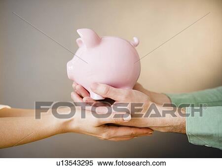 Stock Photography - Close up of man's and woman's hands holding piggy bank, studio shot. Fotosearch