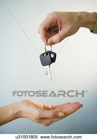 Stock Photography - Close up of man's and woman's hands with car key, studio shot. Fotosearch