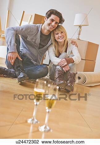 Stock Image - Close up of wine glasses on floor with couple behind. Fotosearch