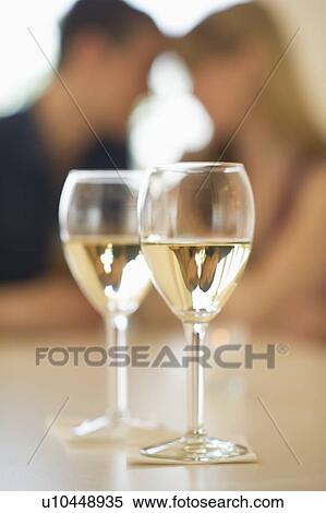 Stock Photography - Close up of wine glasses with couple in background. Fotosearch