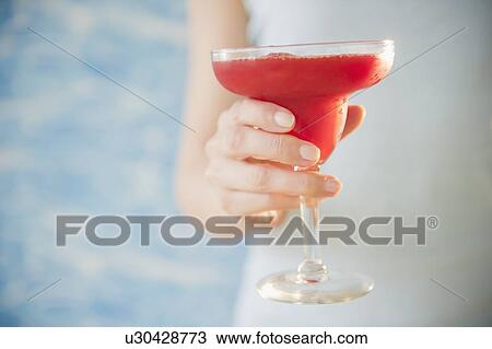 Stock Image - Close up of woman's hand holding cocktail, studio shot. Fotosearch