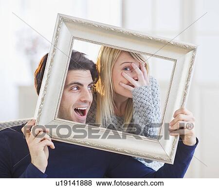 Stock Photo - Couple holding picture frame and making faces. Fotosearch