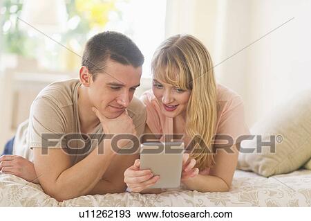 Stock Image - Couple lying on bed and using digital tablet. Fotosearch