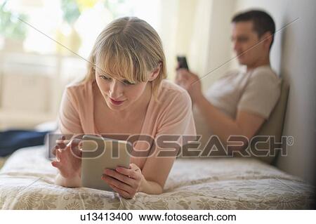 Stock Image - Couple lying on bed and using digital devices. Fotosearch