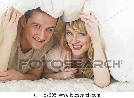 Stock Photo - Couple lying on bed under duvet. Fotosearch