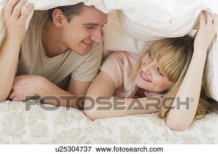 Couple lying on bed under duvet View Large Photo Image Stock Photo - Couple lying on bed under duvet. Fotosearch