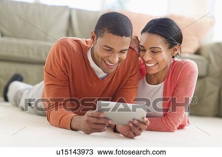 Stock Image - Couple lying on floor reading e-book. Fotosearch