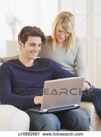 Stock Image - Couple sitting together on armchair and using laptop . Fotosearch