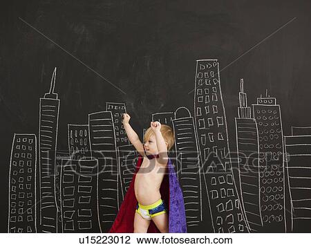 Stock Image - Cute toddler boy (2-3) standing against blackboard with city skyline drawn on it. Fotosearch