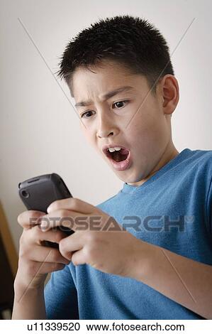 Stock Image - Excited boy (10-11) using mobile phone. Fotosearch