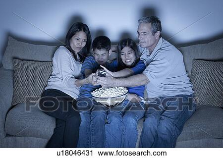 Stock Image - Family sitting on sofa and watching television. Fotosearch