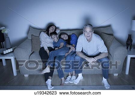 Stock Image - Family sitting on sofa and watching television. Fotosearch