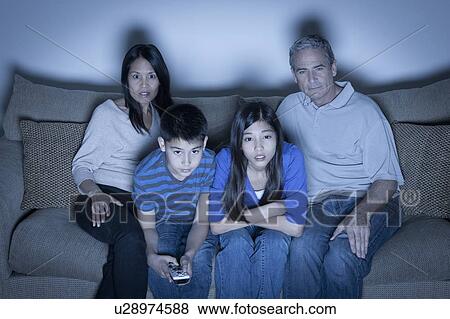 Stock Photo - Family sitting on sofa and watching television. Fotosearch