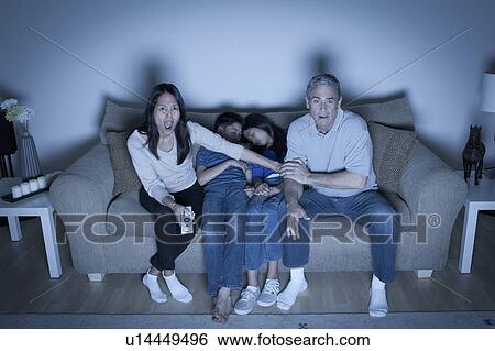 Stock Photograph - Family sitting on sofa and watching television. Fotosearch