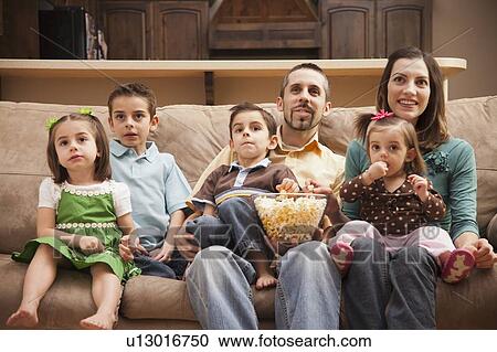 Front view of family with children (18-23 months, 4-5, 6-7, 8-9) sitting on couch watching tv and eating popcorn View Large Photo Image Stock Image - Front view of family with children (18-23 months, 4-5, 6-7, 8-9) sitting on couch watching tv and eating popcorn. Fotosearch
