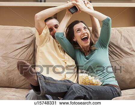 Front view of mid adult couple sitting on couch and fighting for remote control View Large Photo Image Stock Image - Front view of mid adult couple sitting on couch and fighting for remote control. Fotosearch