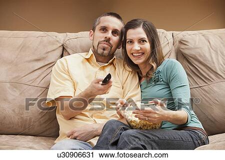 Front view of mid adult couple sitting on couch with remote control and popcorn View Large Photo Image Stock Image - Front view of mid adult couple sitting on couch with remote control and popcorn. Fotosearch