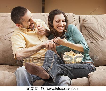 Front view of mid adult couple sitting on couch and fighting for remote control View Large Photo Image Stock Photo - Front view of mid adult couple sitting on couch and fighting for remote control. Fotosearch