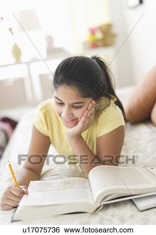 Girl (12-13) lying on bed and studying View Large Photo Image Stock Photograph - Girl (12-13) lying on bed and studying. Fotosearch