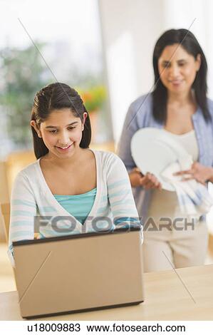 Girl using laptop (12-13) at home, mother in background View Large Photo Image Stock Image - Girl using laptop (12-13) at home, mother in background. Fotosearch