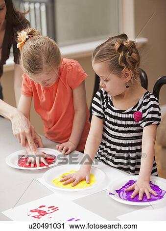 Stock Image - Girls (4-5) holding their hands on plates with paint. Fotosearch