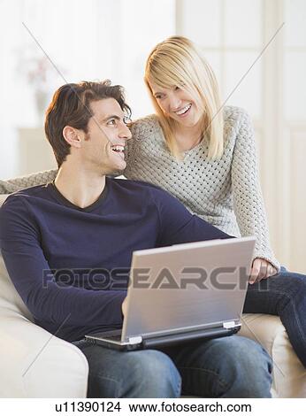 Happy couple sitting together on armchair and using laptop View Large Photo Image Picture - Happy couple sitting together on armchair and using laptop . Fotosearch