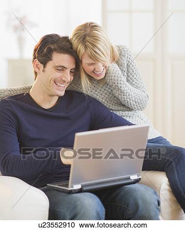 Happy couple sitting together on armchair and using laptop View Large Photo Image Stock Image - Happy couple sitting together on armchair and using laptop . Fotosearch