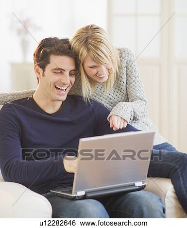 Happy couple sitting together on armchair and using laptop View Large Photo Image Stock Photograph - Happy couple sitting together on armchair and using laptop . Fotosearch