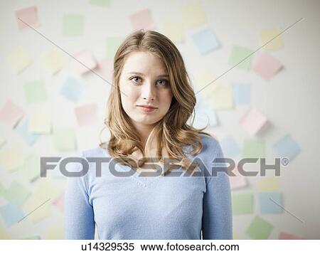 Stock Photography - Indoor portrait of young attractive woman standing in f front of wall covered in adhesive notes. Fotosearch